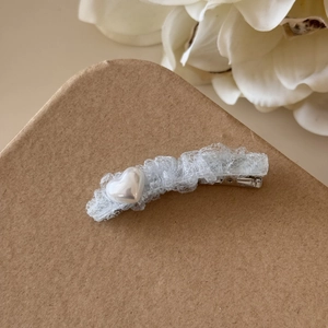 Détail d'une barrette en dentelle bleu clair avec un cœur en perle blanche et clip argenté