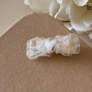 Détail d'une pince à cheveux en dentelle blanche avec cœur perlé sur papier