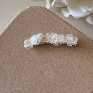 Détail d'une perle en cœur blanche et dentelle crème sur une pince à cheveux en métal