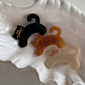 Cute cat-shaped acetate hair clips in black, amber, and beige on a ceramic tray