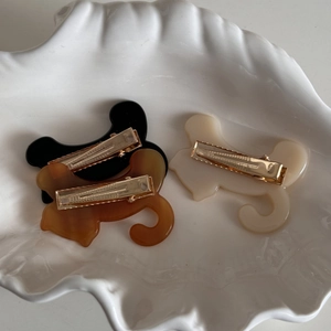 Three acetate cat hair clips in black, amber, and cream white on a ceramic shell plate