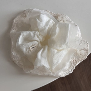Détail d'un chouchou en mousseline blanche avec broderie de dentelle délicate et étiquette