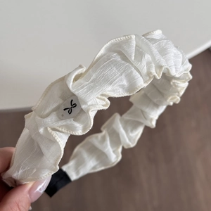 Détail d'un serre-tête blanc en tissu plissé avec logo nœud noir et embouts de protection