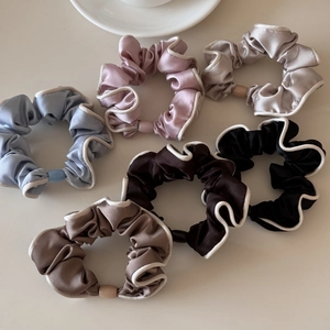Close-up of 6-piece satin hair scrunchies with white contrast piping in various soft colors