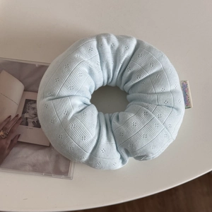 Close-up of a large light blue knitted scrunchie with floral tag on a white table