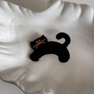 Close-up of black acetate cat hair clip with gold whiskers on white porcelain plate