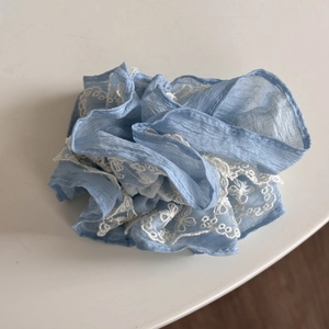 Gros plan du chouchou bleu ciel avec broderie en dentelle blanche et texture de tissu doux