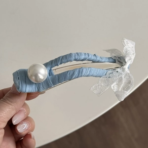 Détail d'une pince à cheveux bleue avec un nœud en dentelle blanche et une perle élégante