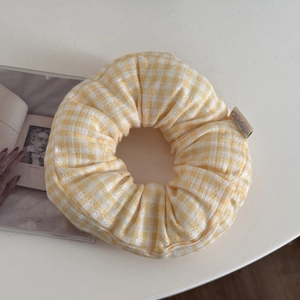 Detail view of a large yellow gingham scrunchie on a white table next to an open book