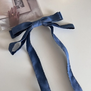 Detailansicht der blauen Denim-Schleife mit braunen Nähten und langen Bändern für Haare