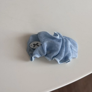 Détail du chouchou bleu clair avec un badge blanc orné d'un motif de nœud noir
