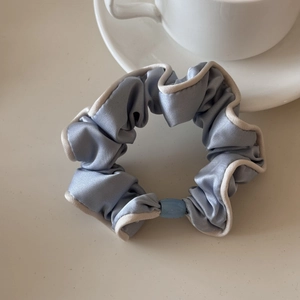 Detail of light blue satin scrunchie with white contrast piping and oval buckle accent