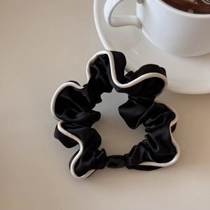 Detail of elegant black satin hair scrunchie with white piping and high-elasticity band