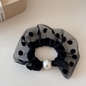 Detail of black polka dot mesh hair scrunchie with large pearl accent on beige surface