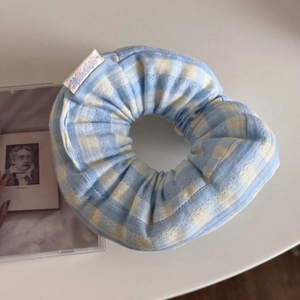 Macro detail of a large blue and white gingham fabric scrunchie with an embroidered tag