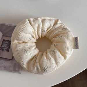 Close-up of beige knit oversized scrunchie featuring grey bow patterns and floral tag