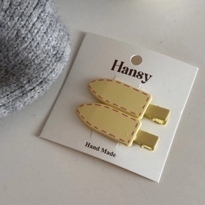 Detail of yellow duckbill hair clips with pink dotted edges on a Hansy paper card