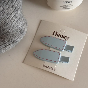 Detail of light blue handmade hair clips with pink stitch patterns on display card
