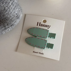 Detail of two mint green hair clips with pink stitching on a white display card