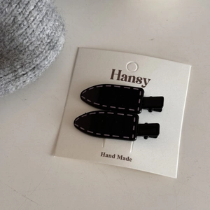 Detail of two black duckbill hair clips with purple stitch design on white card