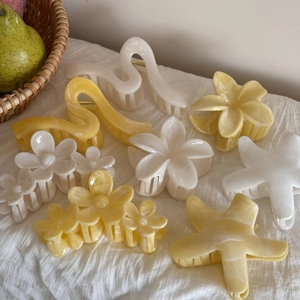 Dettaglio delle mollette per capelli a plumeria e fermagli marmorizzati su lino bianco