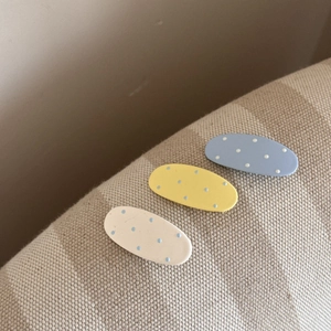 Gros plan de trois barrettes ovales mates à pois en bleu, jaune et beige pastel
