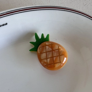 Dettaglio di un fermaglio per capelli a forma di ananas con trama a griglia e finitura lucida