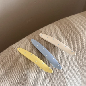 Détail de pinces à cheveux à pois doux en jaune, bleu et blanc sur fond de toile de lin