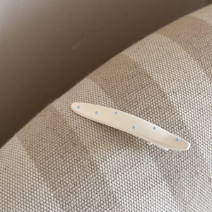Gros plan d'une pince à cheveux blanche à pois bleu clair sur tissu beige