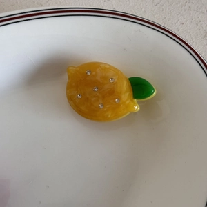 Dettaglio del fermaglio per capelli a limone giallo con foglia verde e strass su piatto