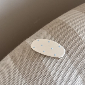 Gros plan sur une barrette ovale à pois bleu clair sur fond blanc avec clip argenté