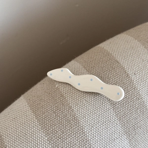 Gros plan d'une pince à cheveux blanche ondulée à pois bleu clair sur tissu
