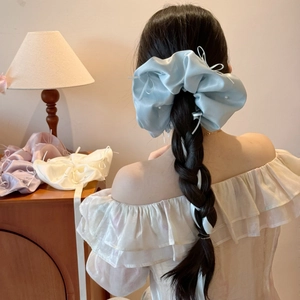 Vue détaillée du chouchou en satin bleu clair avec perles et rubans sur cheveux tressés
