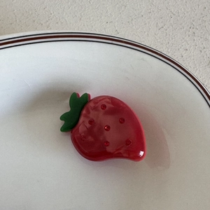 Dettaglio molletta per capelli a fragola con strass rossi su piatto di ceramica bianca