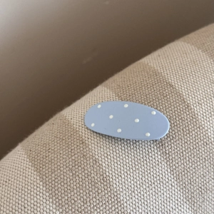Gros plan d'une pince à cheveux mate bleu clair à pois blancs sur tissu rayé