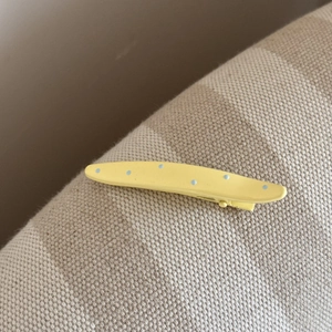 Détail de la barrette bec de canard jaune à pois bleus clairs sur tissu texturé