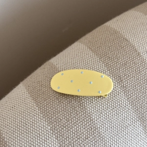 Détail d'une pince à cheveux ovale jaune à pois bleus sur fond de tissu texturé doux