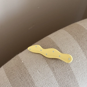 Détail d'une pince à cheveux jaune ondulée à pois bleus sur un tissu en lin