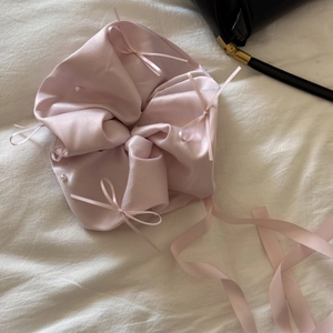 Détail du chouchou en satin rose orné de nœuds et de perles sur tissu blanc