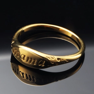 Polished gold stainless steel ring with MAMA engraving and textured edges on black background
