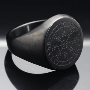 Macro view of a matte black Viking compass ring with engraved runes on stainless steel surface