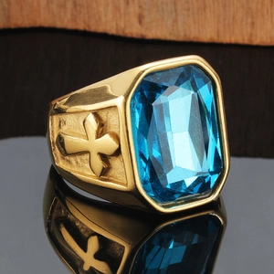 Makroaufnahme eines goldenen Herrenrings mit großem blauem Edelstein und Kreuzreliefs
