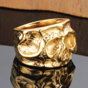 Gouden schedelring in punkstijl met een robuuste gehamerde textuur op een zwart oppervlak