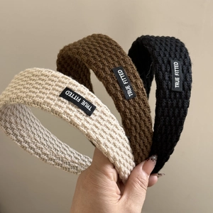 Detail of knitted textured headbands in beige, brown and black with logo patch