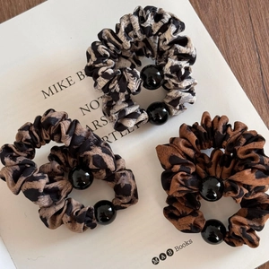Tre elastici per capelli leopardati con perle nere su un elegante display di libri