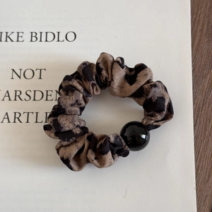 Dettaglio dell'elastico per capelli leopardato con perla nera lucida e tessuto elastico