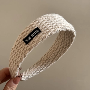Close-up of beige knitted headband featuring a black TRUE FITTED patch and textured wool