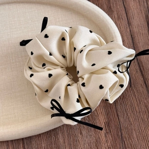 Nahaufnahme von cremefarbenem Scrunchie mit schwarzen Herzen und Schleifen auf Tablett