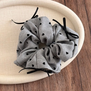 Detail eines grauen Scrunchies mit Herzmuster und Schleifen in einem Dekotablett