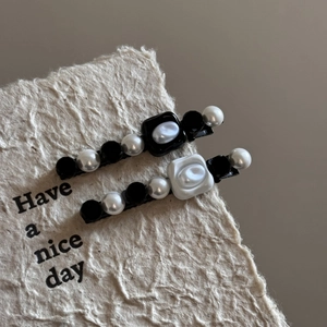 Detail view of pearl hair clips with white rose and black geometric shapes on beige paper